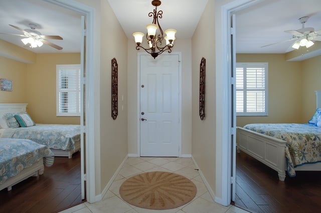 Tiled entry hall with a round rug and chandelier, flanked by two bedrooms with ceiling fans and floral bedding
