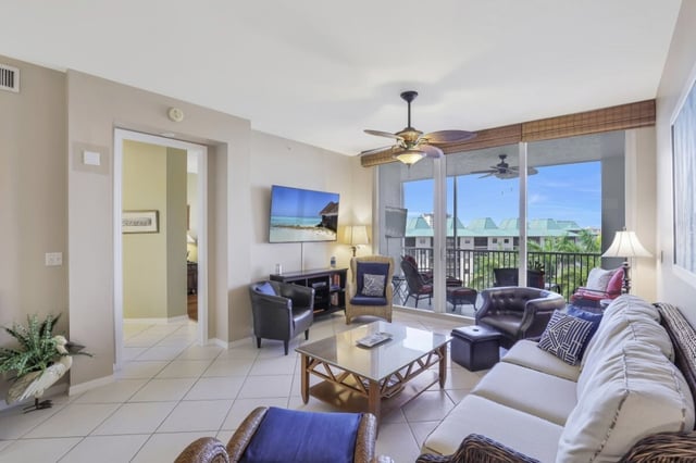 Bright condo living room with ceiling fan, wall-mounted TV and sliding doors opening to a balcony with rooftop views