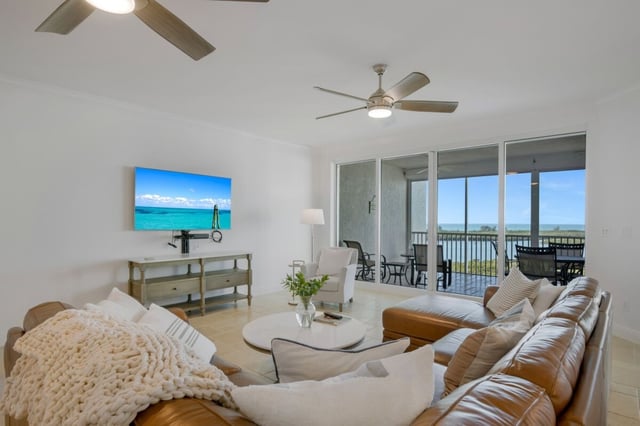Bright condo living room with leather sectional, ceiling fans and sliding glass doors opening to a water-view balcony