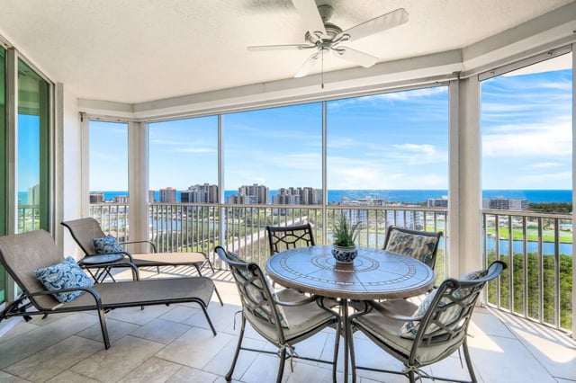 Screened high-rise balcony with patio table, lounge chairs and ceiling fan overlooking golf course and Gulf coastline
