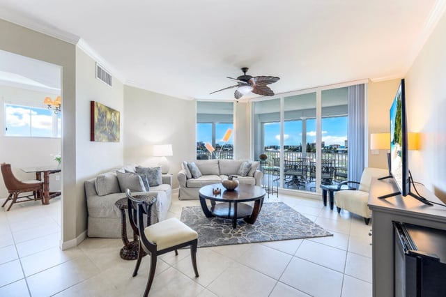 Bright condo living room with cream sofas, round coffee table and floor-to-ceiling windows opening to a waterfront balcony