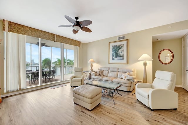 Bright condo living room with cream leather sofa, recliners and sliding doors opening to a waterfront balcony