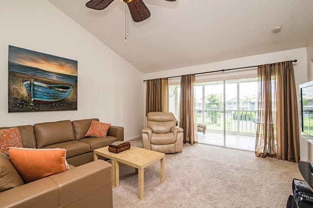 Bright living room with tan sofas, orange pillows, a boat painting, and sliding glass doors to a screened lanai
</result>