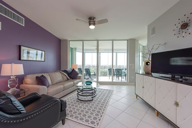 Condo living room with purple accent wall, beige sofa, ceiling fan and sliding glass doors to a balcony
