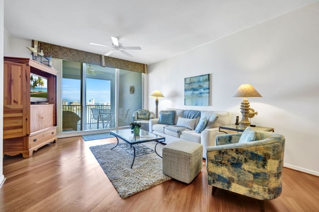 Condo living room with hardwood floors, ceiling fan, and sliding glass doors opening to a balcony with water views