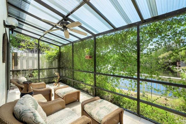 Screened lanai with wicker furniture, palm-print cushions and ceiling fan overlooking greenery and a lake