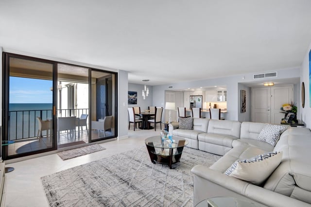 Open condo living room with white sectional sofa, glass coffee table and sliding doors to a Gulf-view balcony