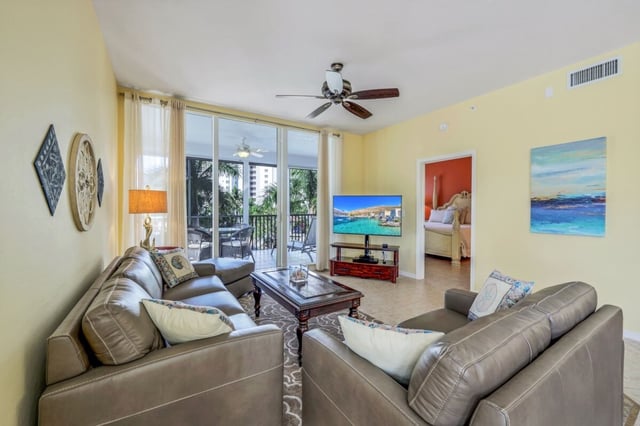 Condo living room with leather sectional sofas, ceiling fan, flat-screen TV and sliding doors to a balcony