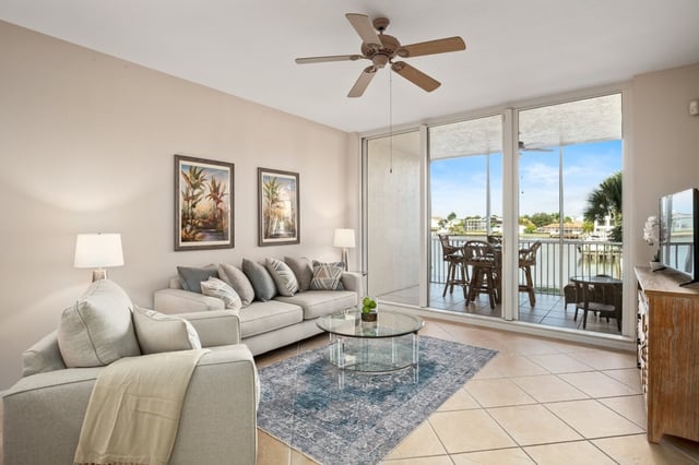 Bright condo living room with sectional sofa, glass coffee table and sliding doors to a balcony overlooking the water