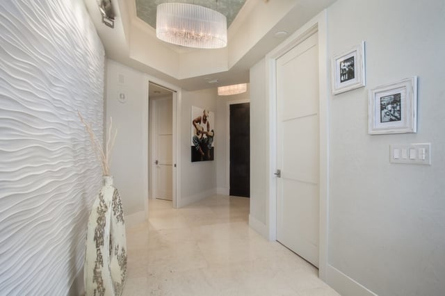 Bright white hallway with wavy textured accent wall, drum chandelier, marble floors and framed artwork