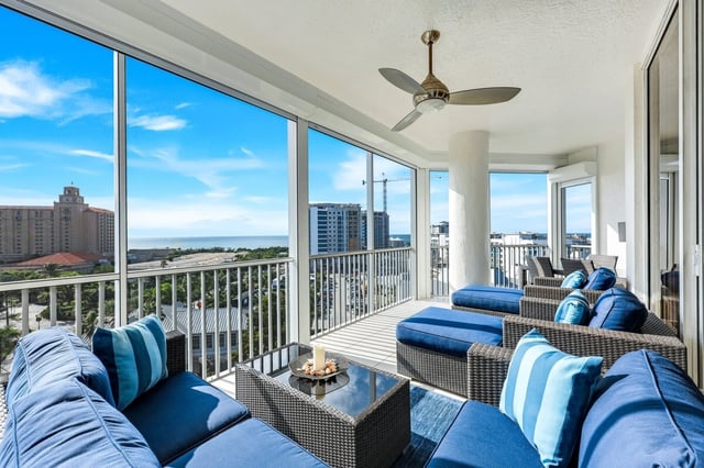 Screened high-rise balcony with blue wicker seating, ceiling fan, and sweeping Gulf and city views