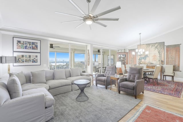Bright open living room with sectional sofa, ceiling fan, dining area and sliding glass doors to a water view