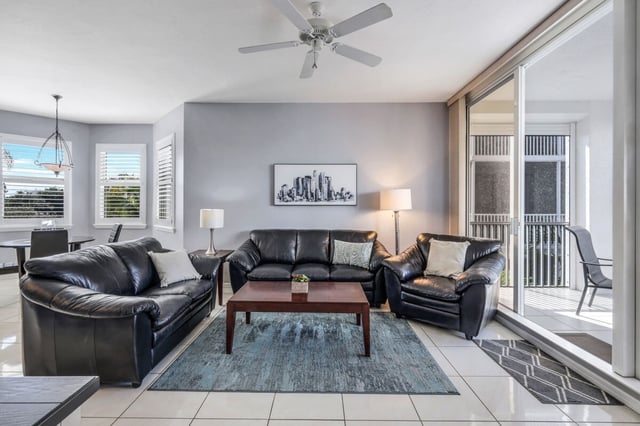 Condo living room with black leather sofas, gray walls, ceiling fan and sliding glass doors to a balcony