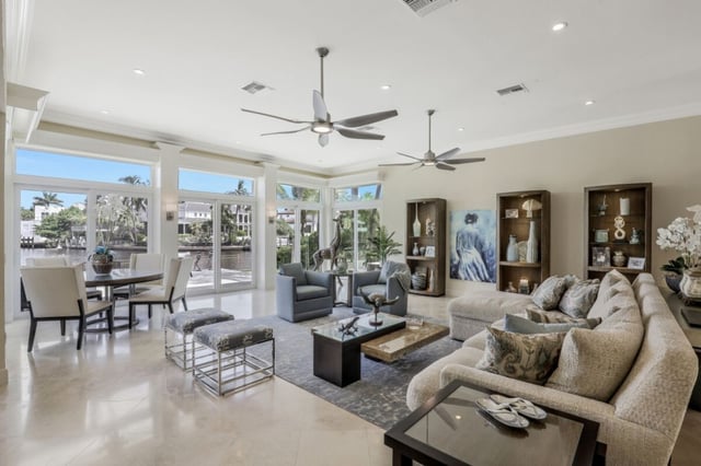 Open-plan living and dining room with ceiling fans, cream sofas and marble floors overlooking a waterfront view