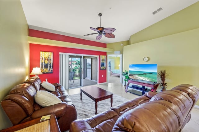 Condo living room with brown leather sofas, red accent wall, palm-leaf ceiling fan and sliding doors to a balcony