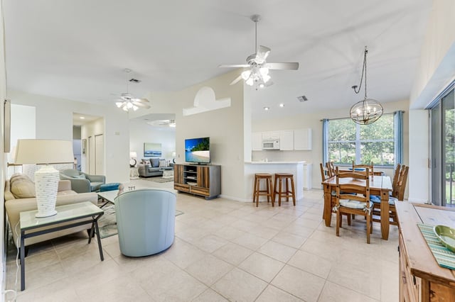 Open-concept living and dining area with tile floors, ceiling fans, breakfast bar stools and a bright kitchen