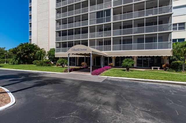 Entrance canopy marked 5 Bluebill Avenue at a multi-story Naples condominium with palms and pink flower beds