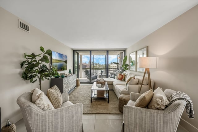 Bright coastal condo living room with woven armchairs, wall-mounted TV and sliding doors to a balcony with water views