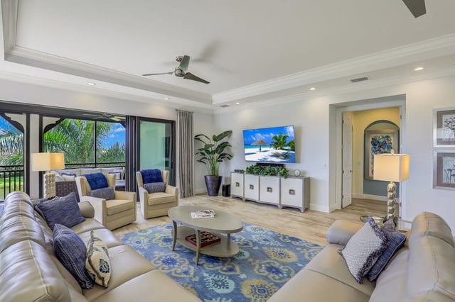 Bright coastal living room with sectional sofa, blue patterned rug, wall-mounted TV and sliding doors to a screened lanai