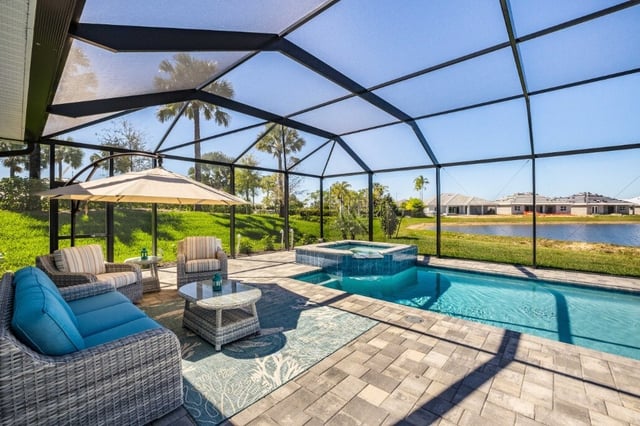 Screened lanai with pool, raised spa, wicker lounge seating and umbrella overlooking a lake and palm trees