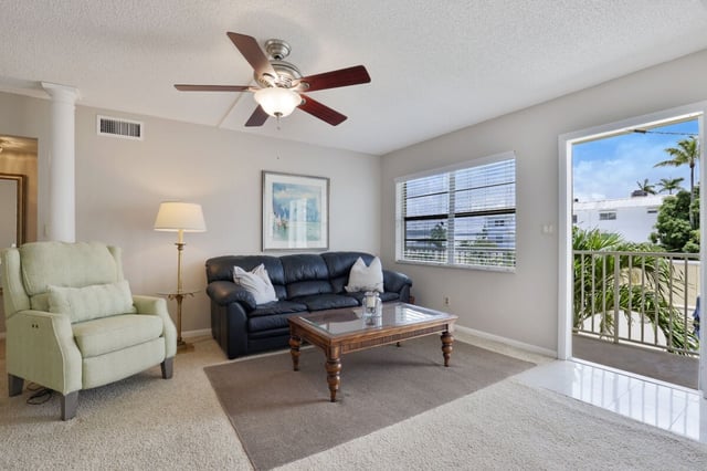 Condo living room with navy leather sofa, wooden coffee table and ceiling fan beside a sunny balcony doorway