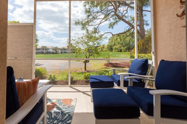 Screened lanai with navy cushioned chairs overlooking a pond, golf course lawn and pine trees