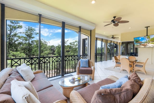 Screened lanai with wicker sofas, ceiling fans and a dining set overlooking treetops under blue sky