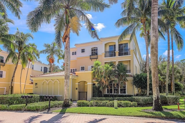 Yellow Mediterranean-style condo building with balconies, tile roof and palm trees under a blue sky