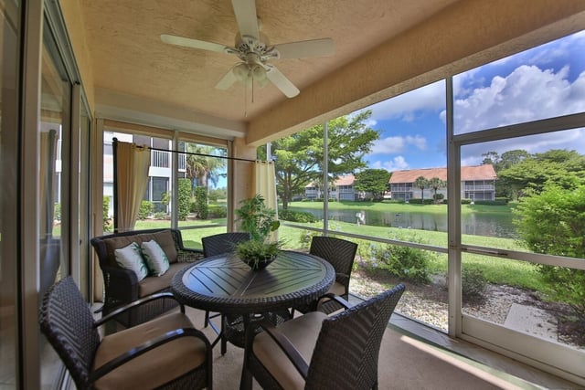 Screened lanai with wicker table and chairs, ceiling fan, and views of a lake and palm-lined condos