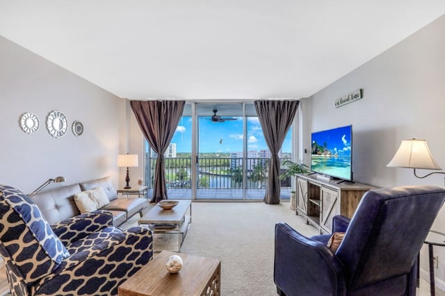 Condo living room with patterned sofa, navy armchairs and sliding glass doors opening to a balcony with water views