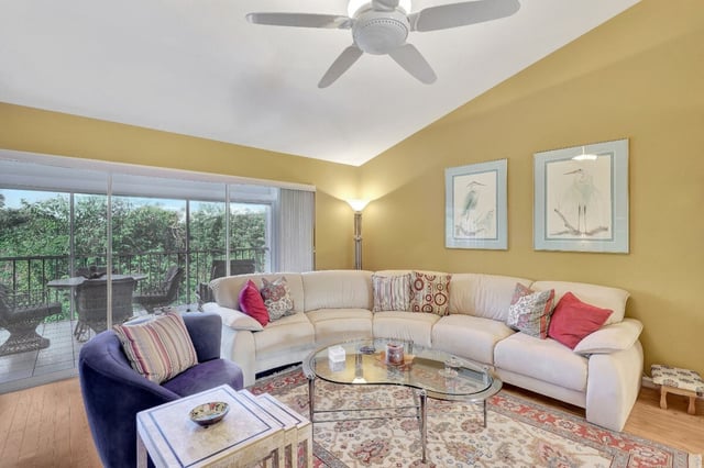 Bright living room with a cream sectional sofa, purple armchair, glass coffee table and heron prints on yellow walls