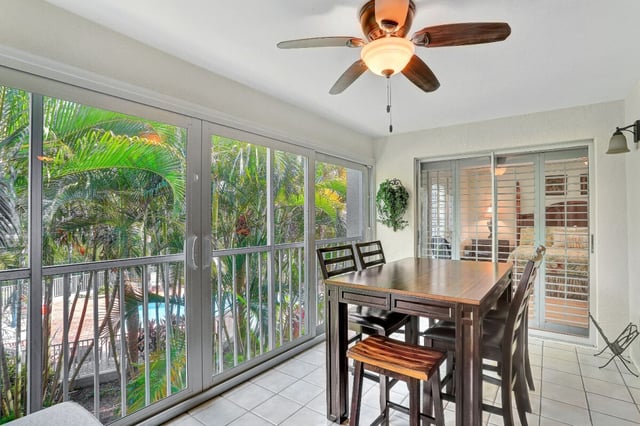 Screened lanai with a high-top wood table, stools, ceiling fan and palm views over a pool below