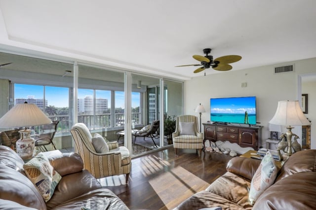 Condo living room with leather sofas, palm-leaf ceiling fan, flat-screen TV and sliding doors to a sunny balcony view