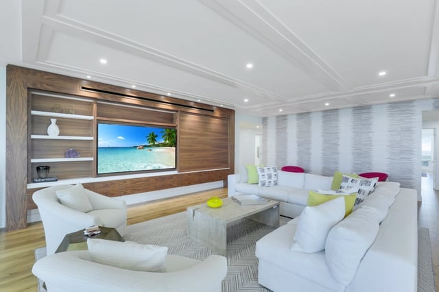 Bright modern living room with white sectional sofas, walnut media wall and large screen showing a beach scene