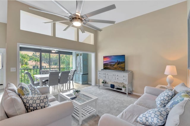 Bright condo living room with vaulted ceiling, ceiling fan, white sofas and sliding doors to a screened lanai