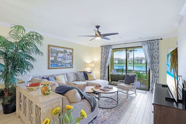 Bright condo living room with sectional sofa, ceiling fan and sliding glass doors opening to a lake view