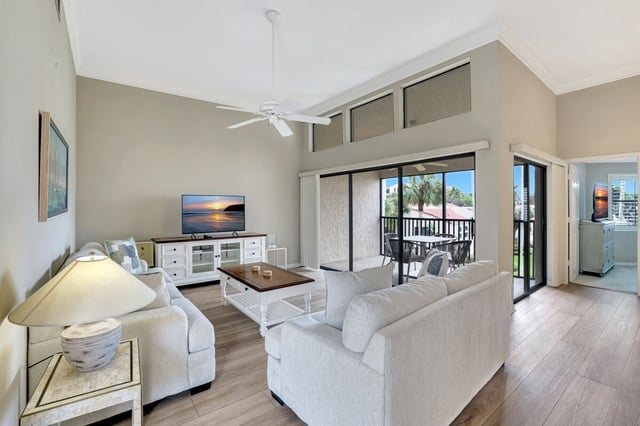 Bright condo living room with vaulted ceiling, ceiling fan, white sofas and sliding doors to a balcony