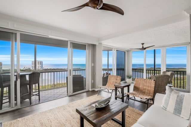 Bright condo living room with ceiling fan, woven chairs and sliding glass doors opening to a Gulf-view balcony