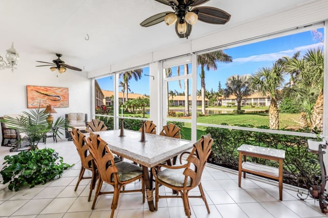 Screened lanai with rattan dining set, ceiling fans and tile floor overlooking palm trees and green lawn
Sun-filled screened lanai with a rattan dinin