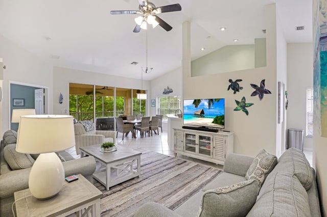 Bright coastal living room with vaulted ceiling, ceiling fan, gray sectional, sea turtle and starfish wall decor