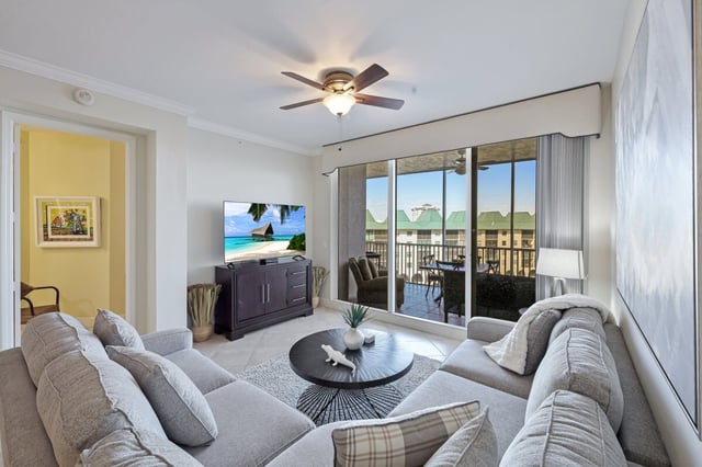 Bright condo living room with gray sectional sofa, ceiling fan, flat-screen TV and sliding doors to a screened balcony