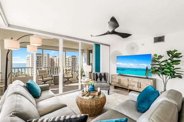 Bright condo living room with teal accents, wicker coffee table and sliding doors to a balcony with Gulf views