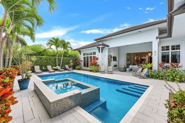 Backyard pool and raised spa at a white Naples home with palms, lounge chairs and a covered lanai
- Describe what is visible: setting, people, food, w