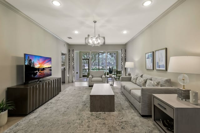 Modern living room with gray sectional sofa, wall-mounted TV, drum chandelier and sliding doors to a green view