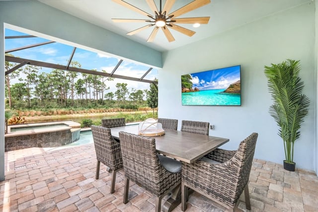 Covered lanai with wicker dining set, ceiling fan, wall-mounted TV and screened pool area overlooking pines