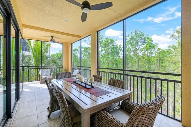 Screened lanai with wicker dining chairs, ceiling fan and views of palms and woodland under a blue sky