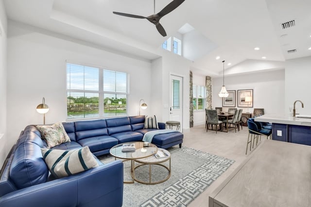 Bright open-plan living room with blue leather sectional, glass coffee table, and dining area beside a white kitchen island