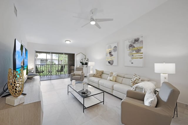 Bright condo living room with beige sectional, glass coffee table, ceiling fan and sliding doors to a screened lanai