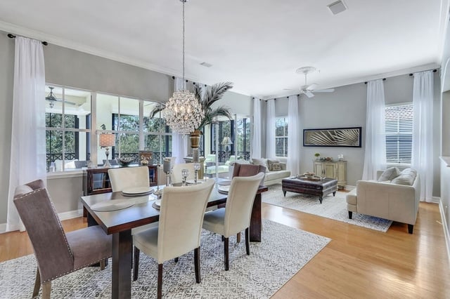 Open-plan dining and living room with crystal chandelier, upholstered chairs and sunlit windows with white curtains