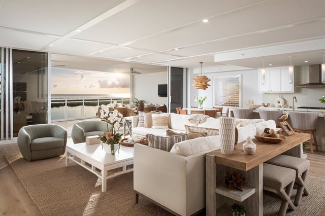 Open-plan coastal living room with white sectional, swivel chairs and a dining table framing water views at sunset